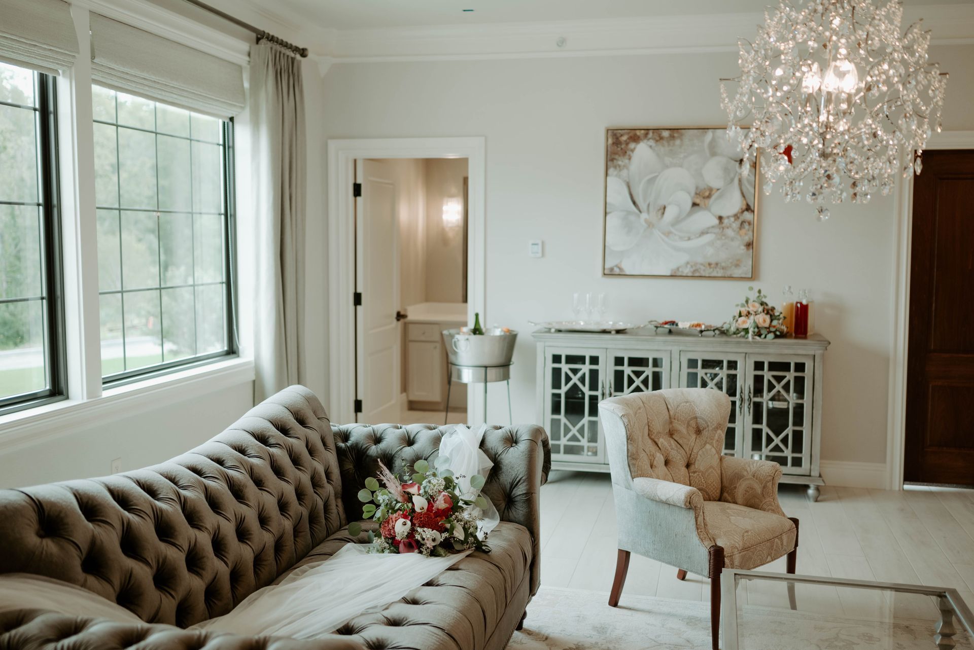 Elegant room with tufted sofa, floral arrangement, armchair, and crystal chandelier.