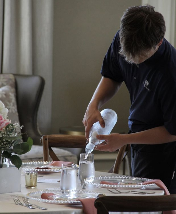 Person pouring water into a glass at a table set for a meal.