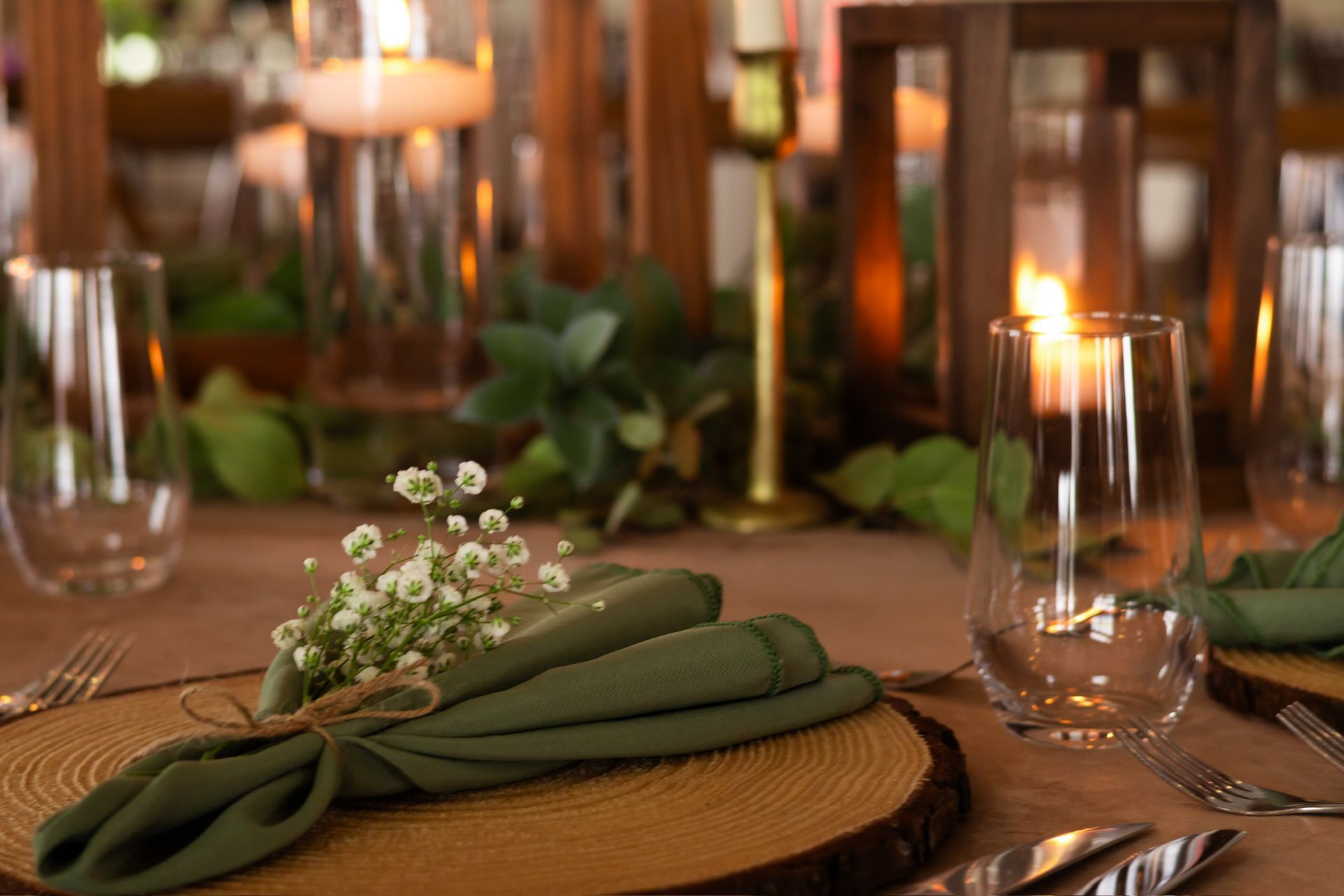 Table setting with green napkins, wooden chargers, clear glassware, and candles.