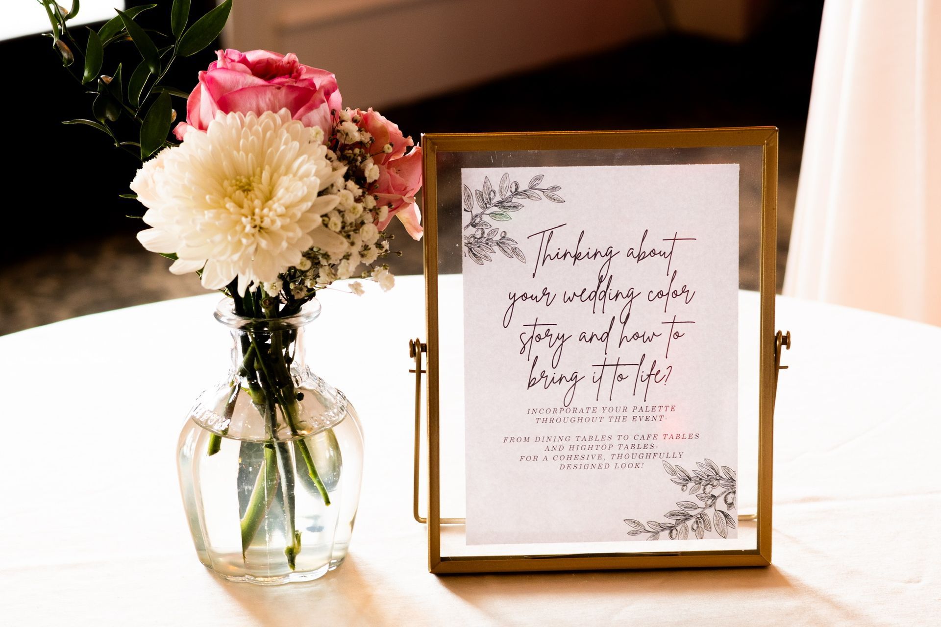 A framed sign with floral accents next to a vase of flowers on a table.