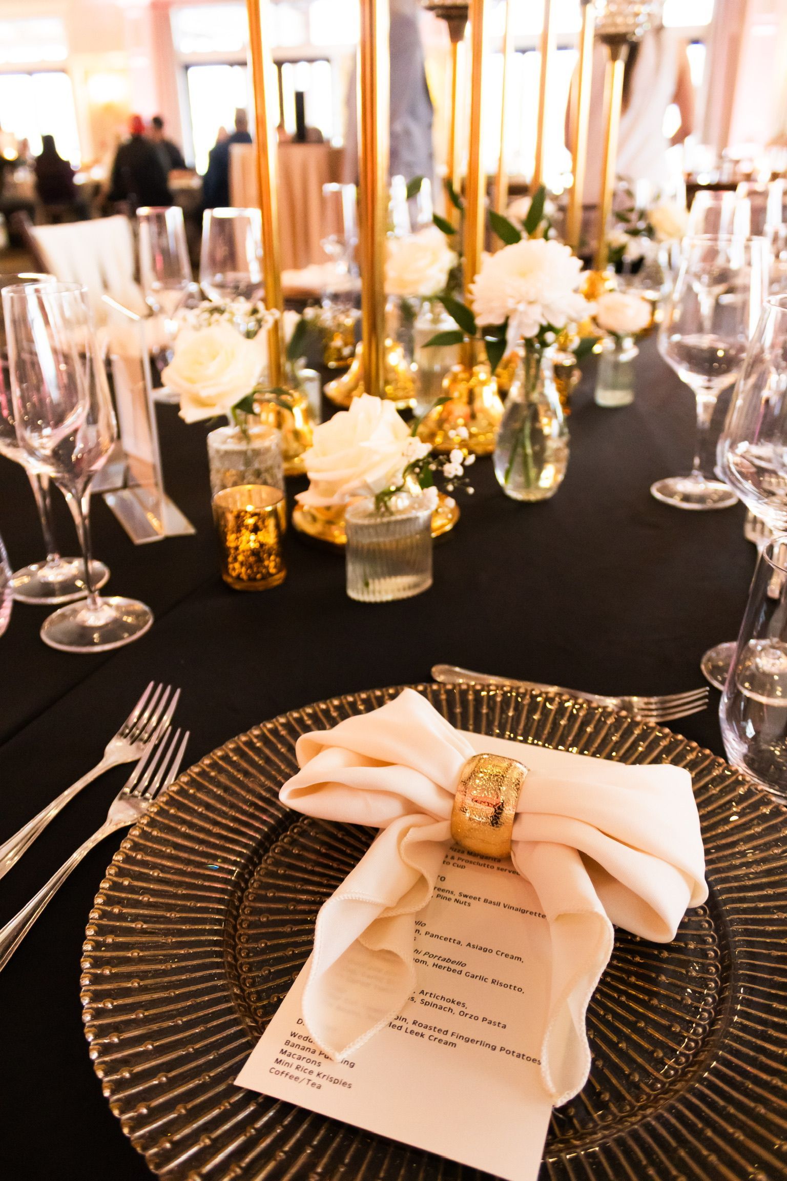 Elegant table setting with gold accents, white flowers, and black tablecloth.