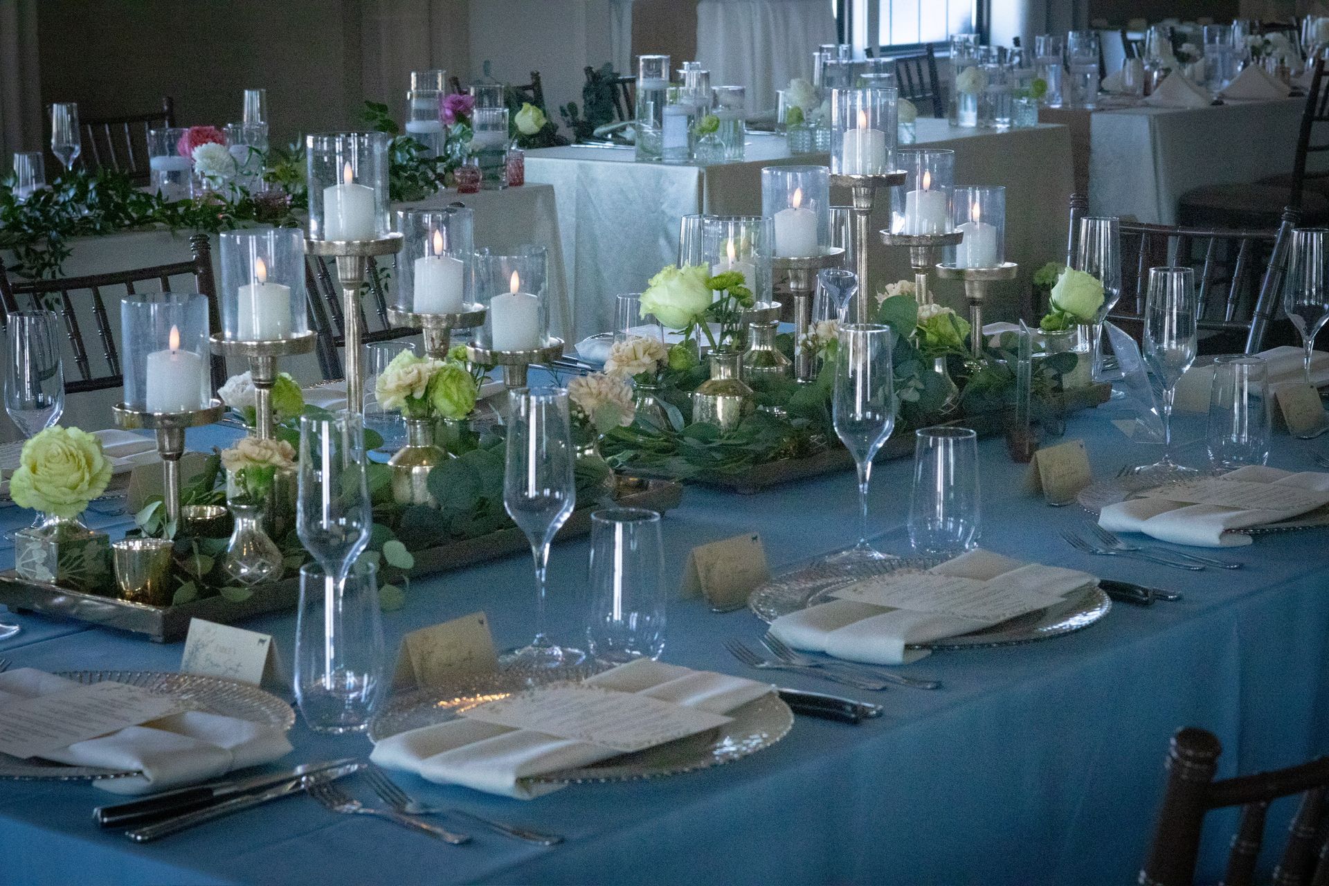 Wedding reception table setting with floral centerpieces, candles, and blue tablecloth.