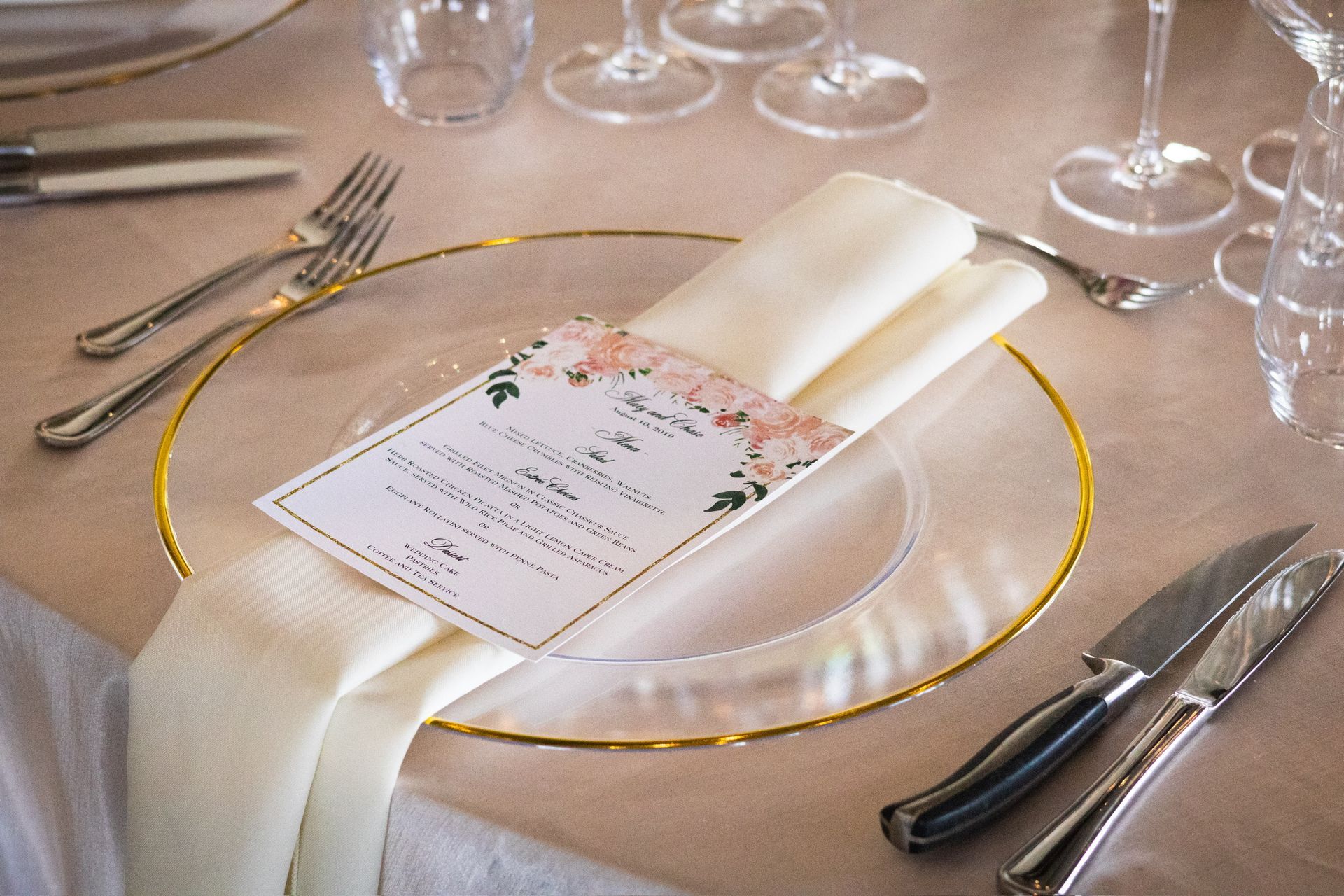 Place setting with gold-rimmed clear plate, menu, cream napkin, and silverware.