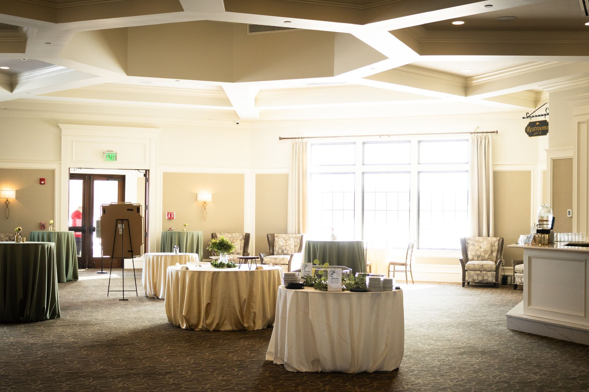 Elegant event space with round tables covered in various colors. Window provides natural light.