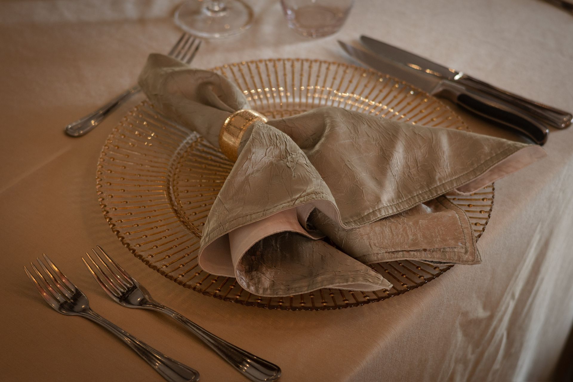 Formal table setting with gold charger plate, napkin, and silverware.