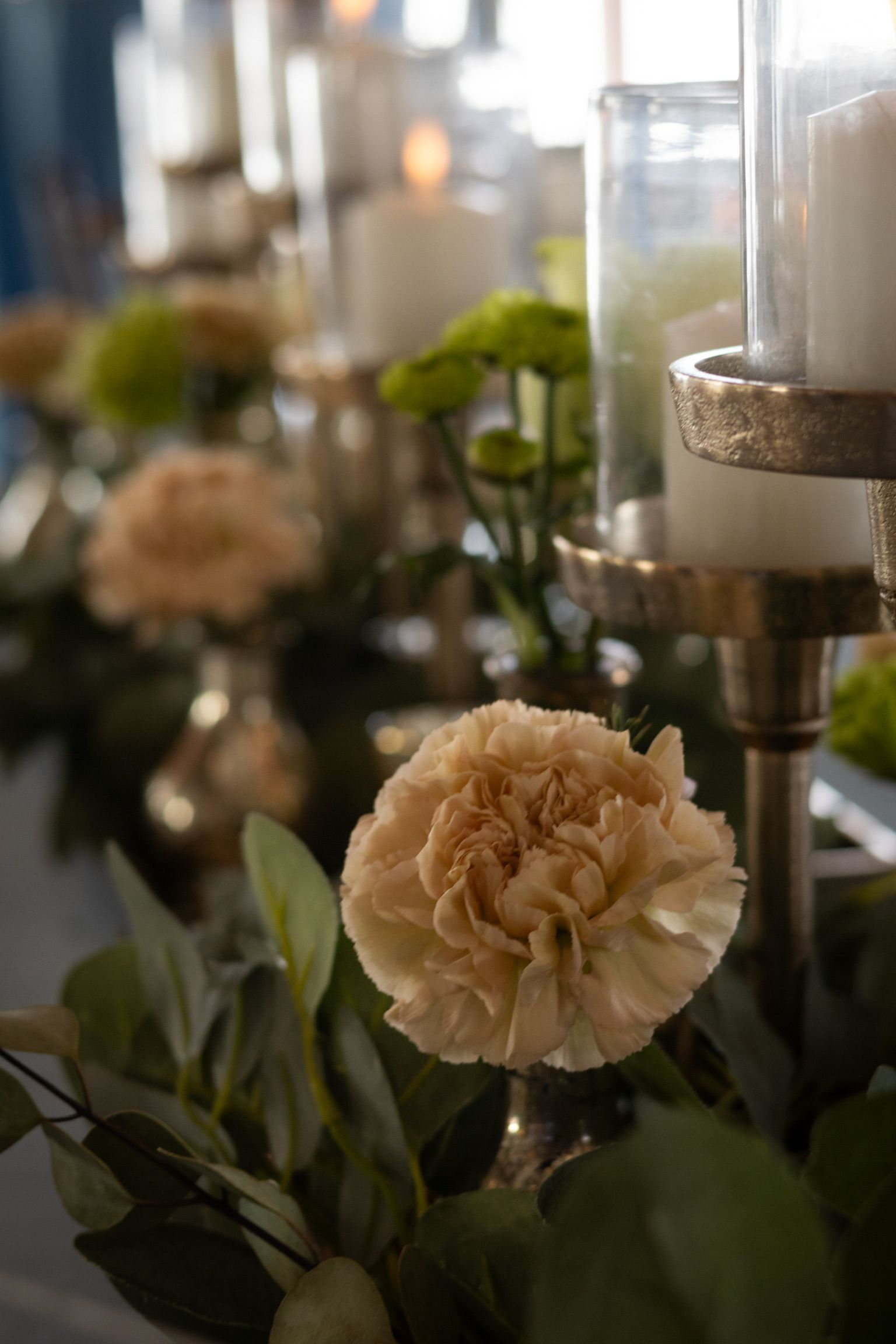 Cream-colored flowers and greenery decorate a table with silver candle holders and lit candles.