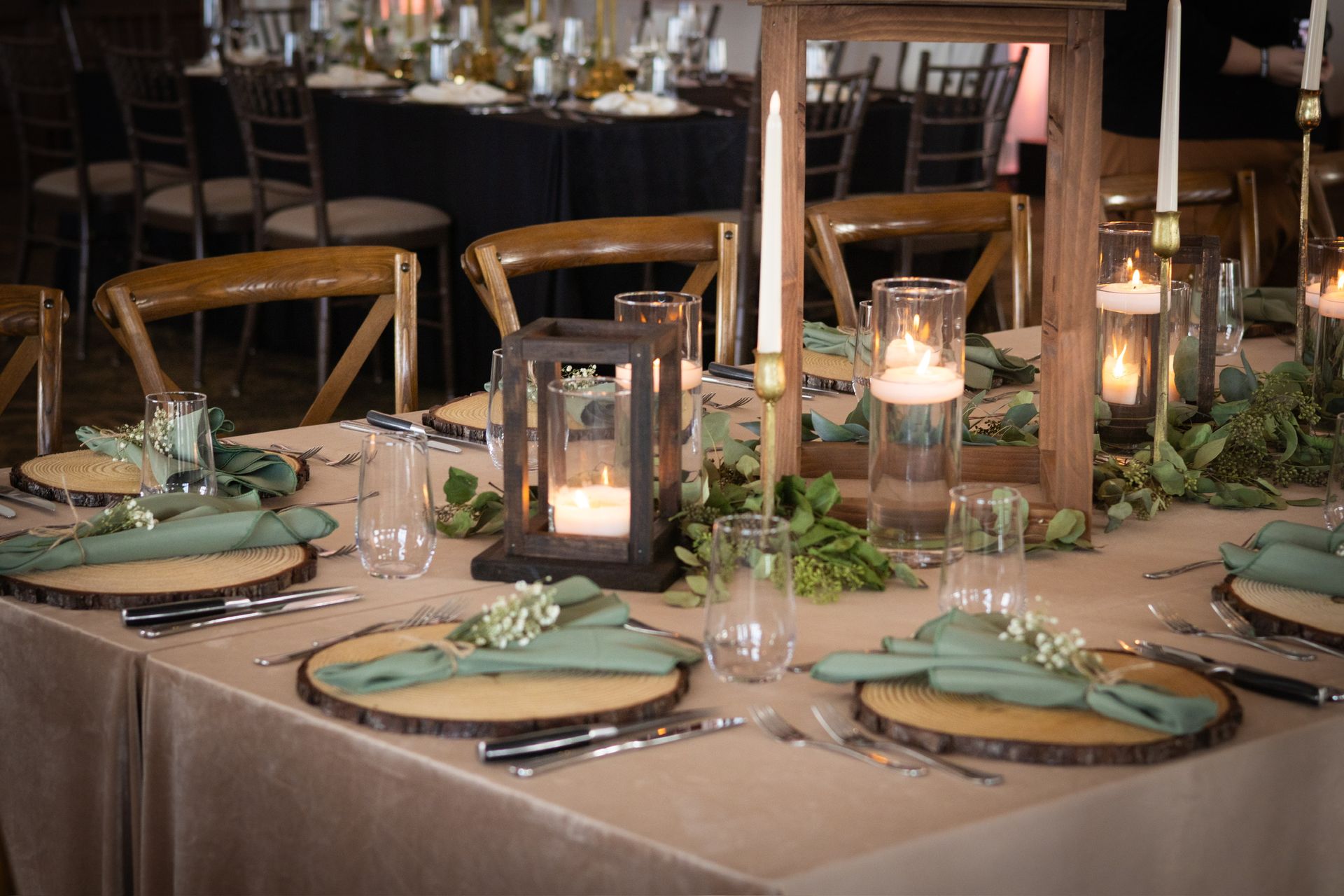 Wedding reception table setting with candles, greenery, wood chargers, and green napkins.