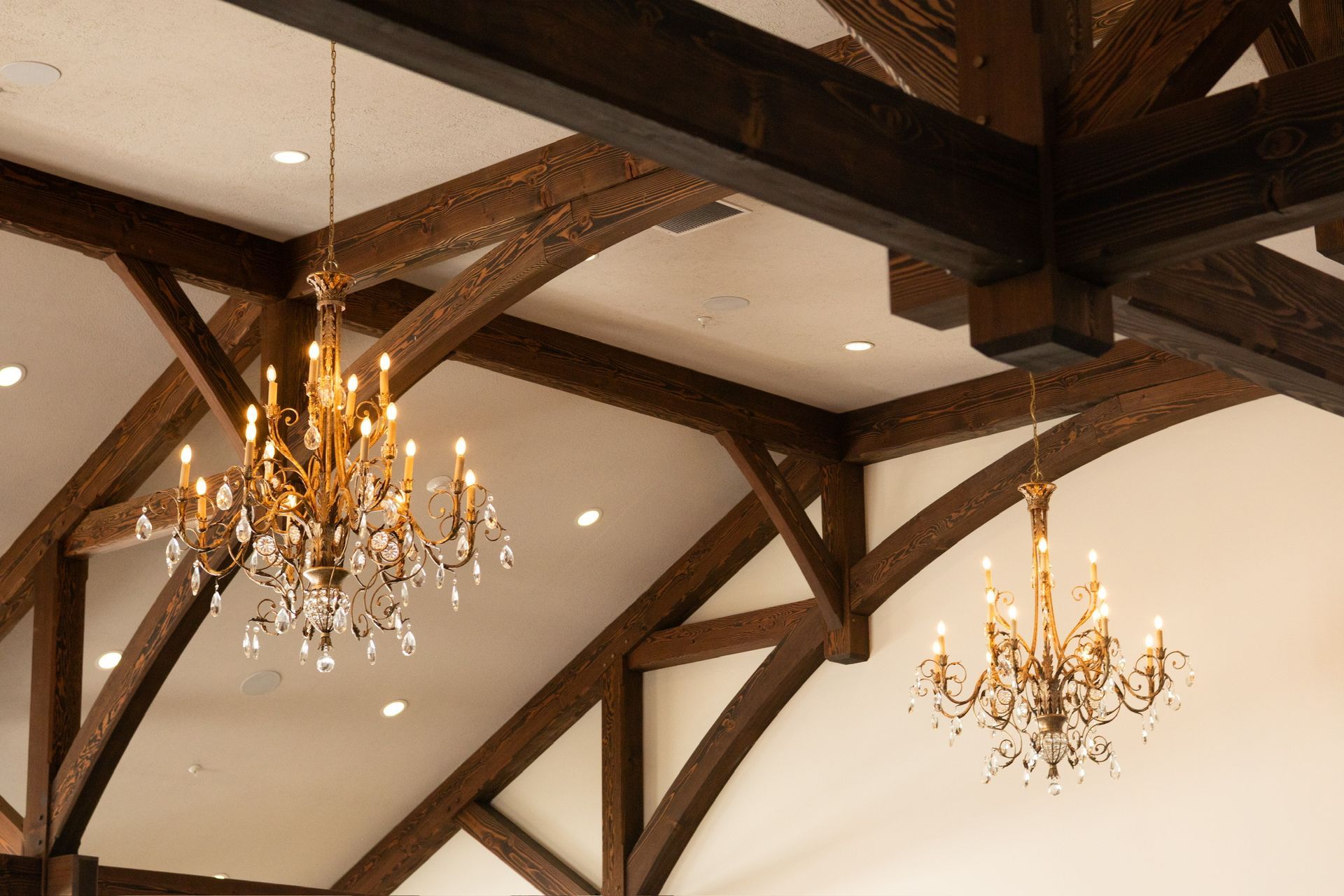 Two ornate chandeliers hang from a high ceiling with exposed wooden beams.