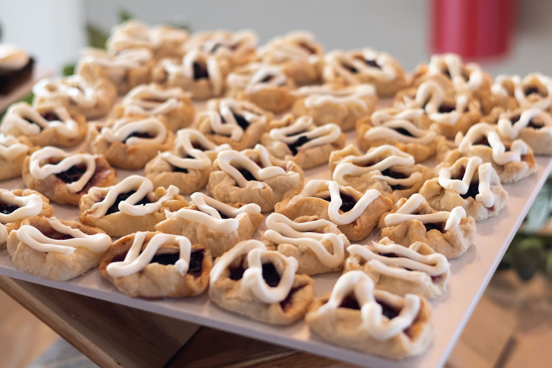 Tray of small pastries with dark filling and white icing drizzle.