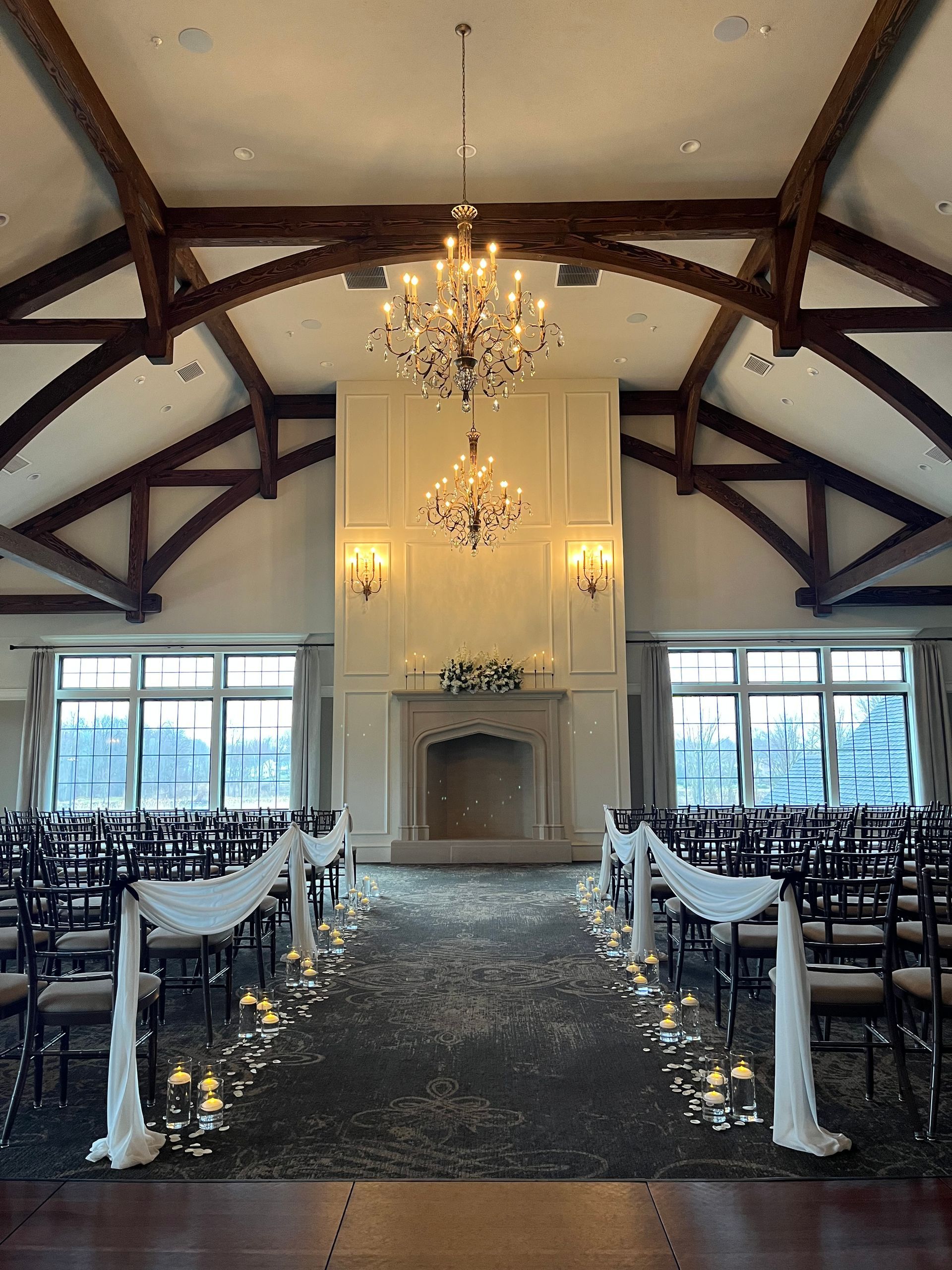 Wedding ceremony setup with draped aisle, candles, fireplace, and chandeliers.