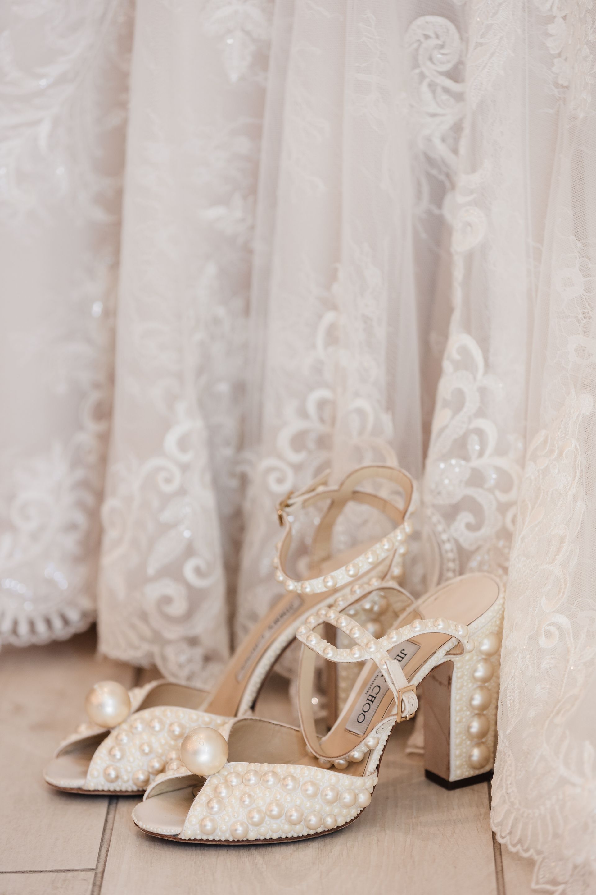 Ivory pearl-covered bridal shoes with thick heels, next to white lacy wedding dresses.