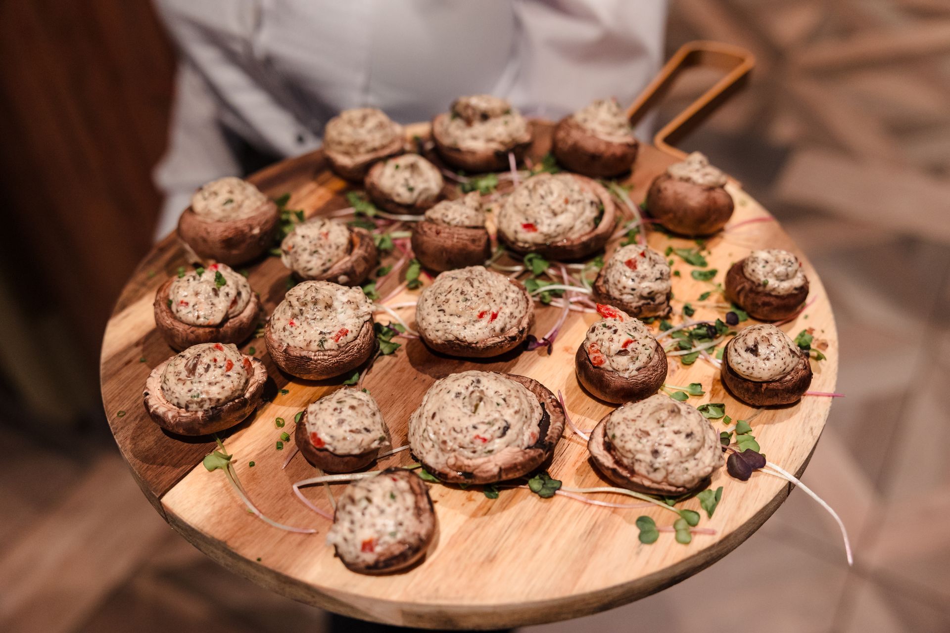 Stuffed mushrooms on a wooden serving board, held by a person.