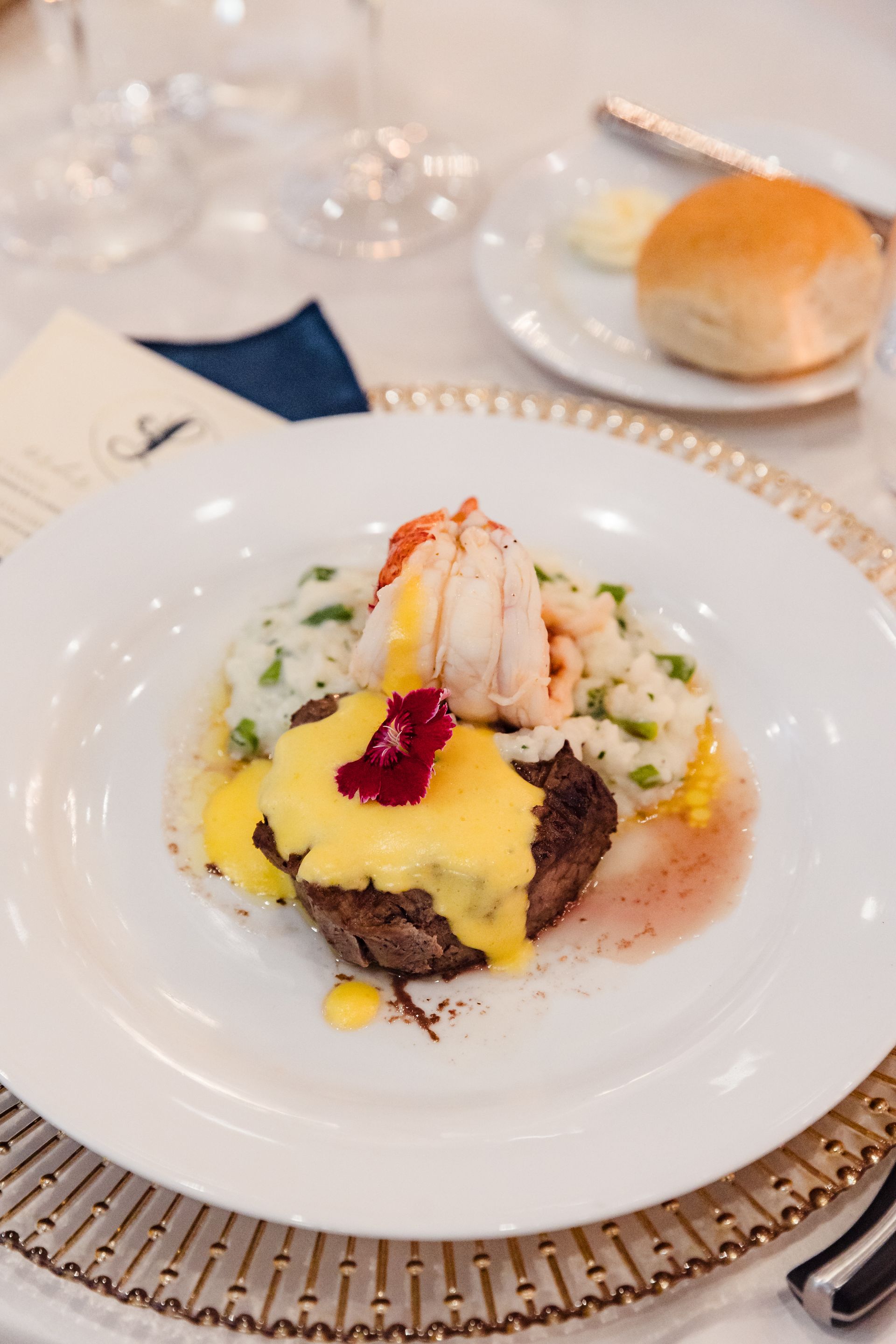 Steak and lobster with sauce and mashed potatoes on a white plate, served with a roll.