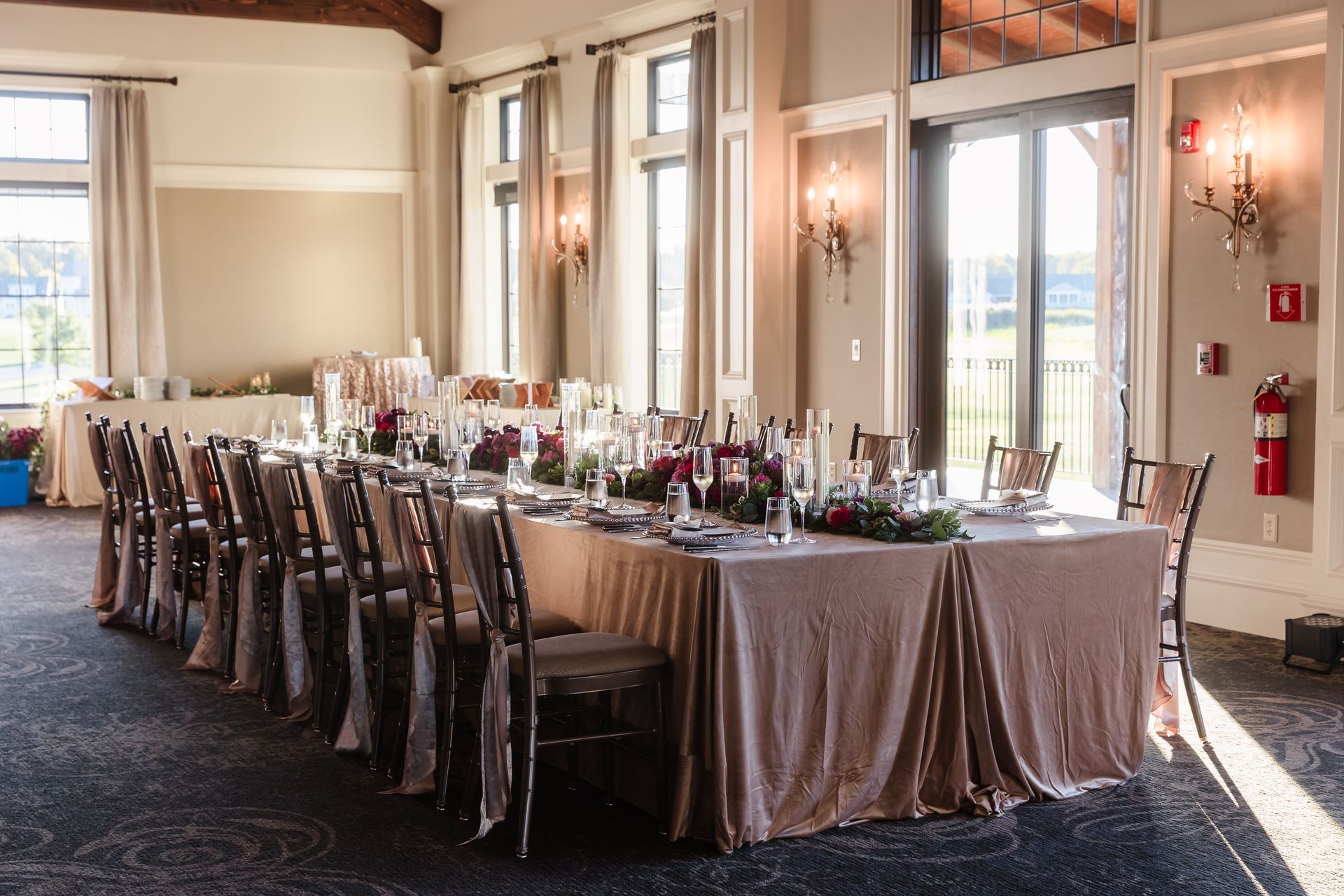 Long dining table set for a formal event, with floral centerpieces, in a well-lit room.