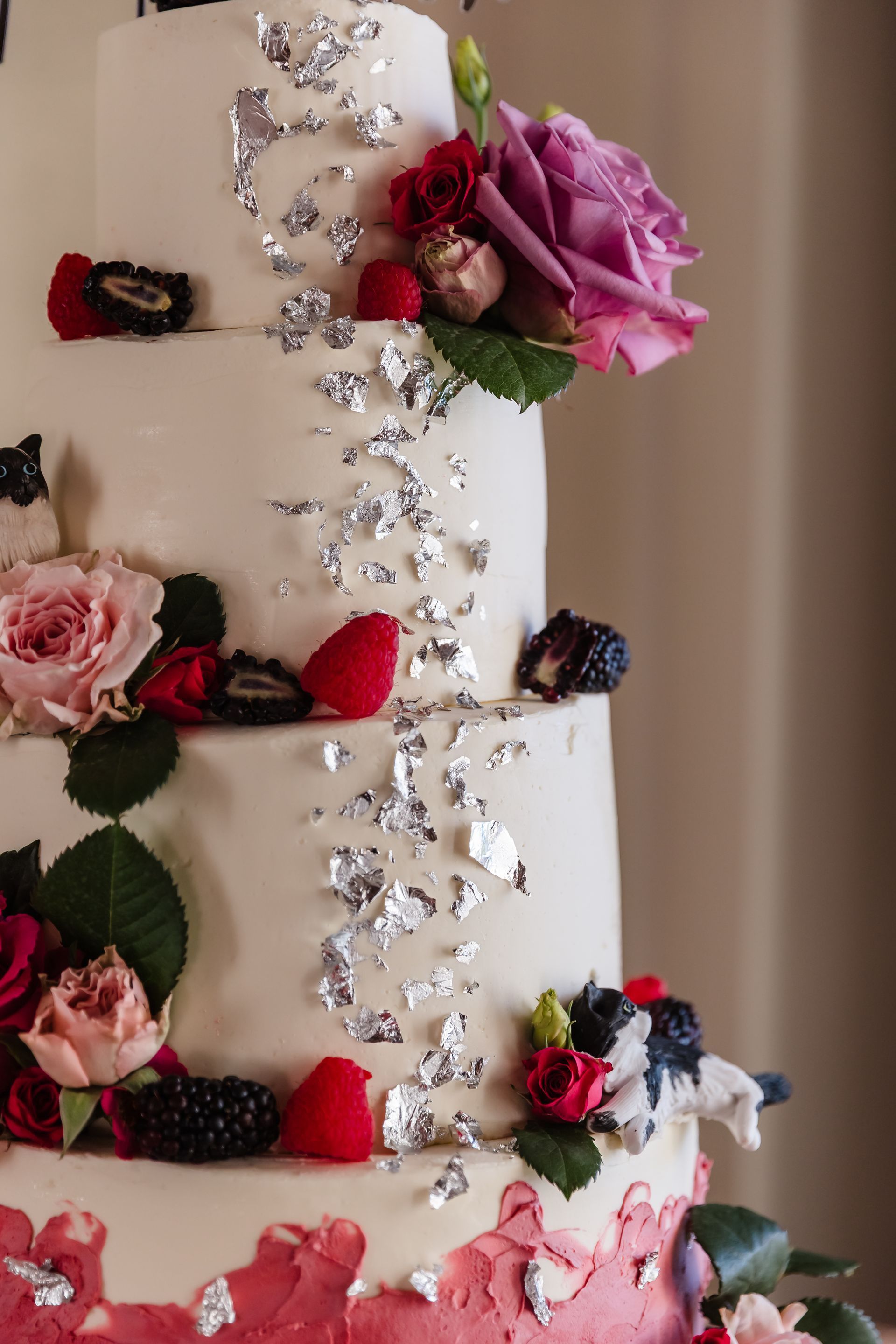 Four-tiered white cake with red and silver accents, decorated with flowers and berries.