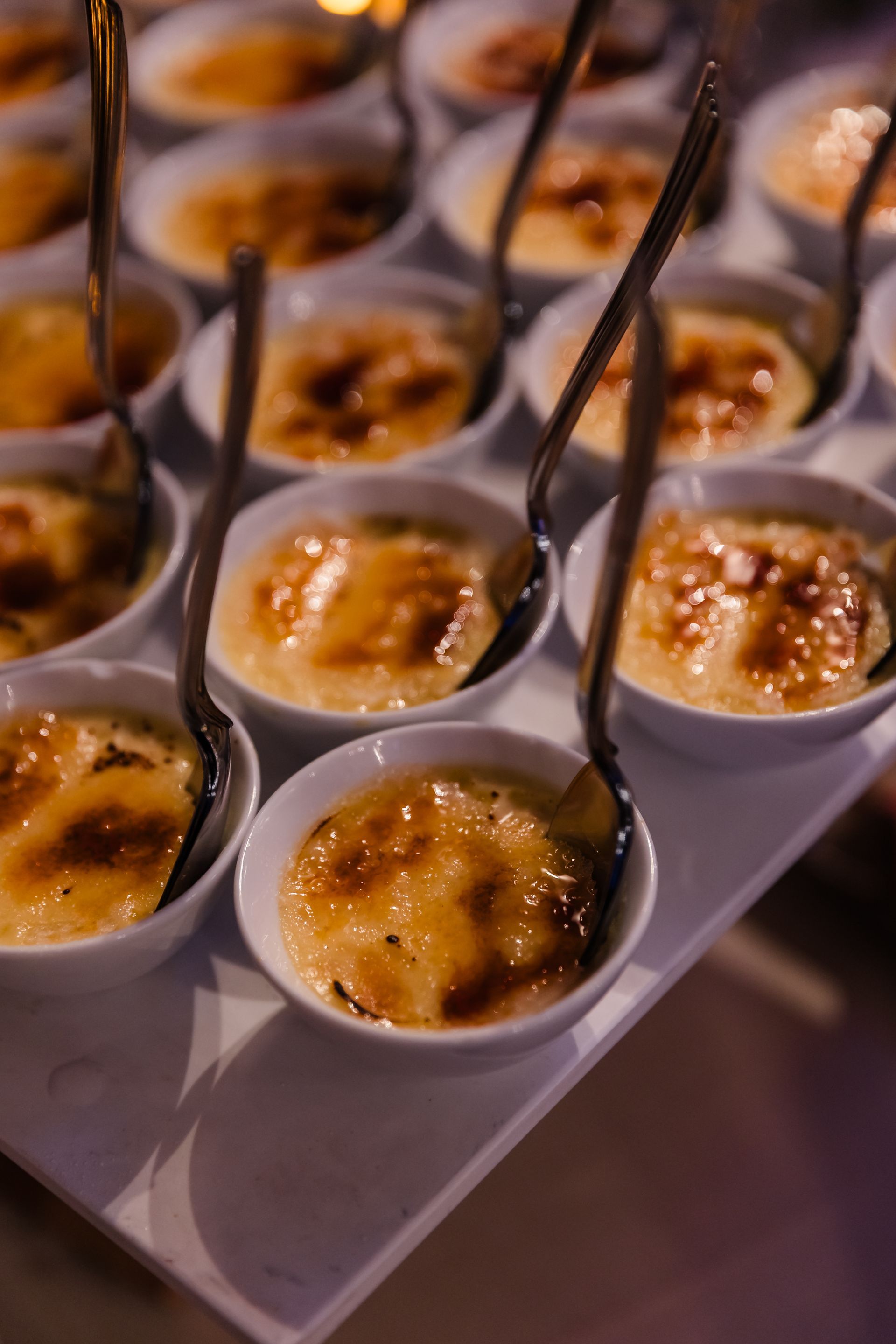 Tray of crème brûlée desserts with caramelized sugar tops in white bowls, spoons included.