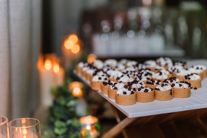 Tray of mini tarts with cream filling and chocolate chips, candles and greenery in the background.