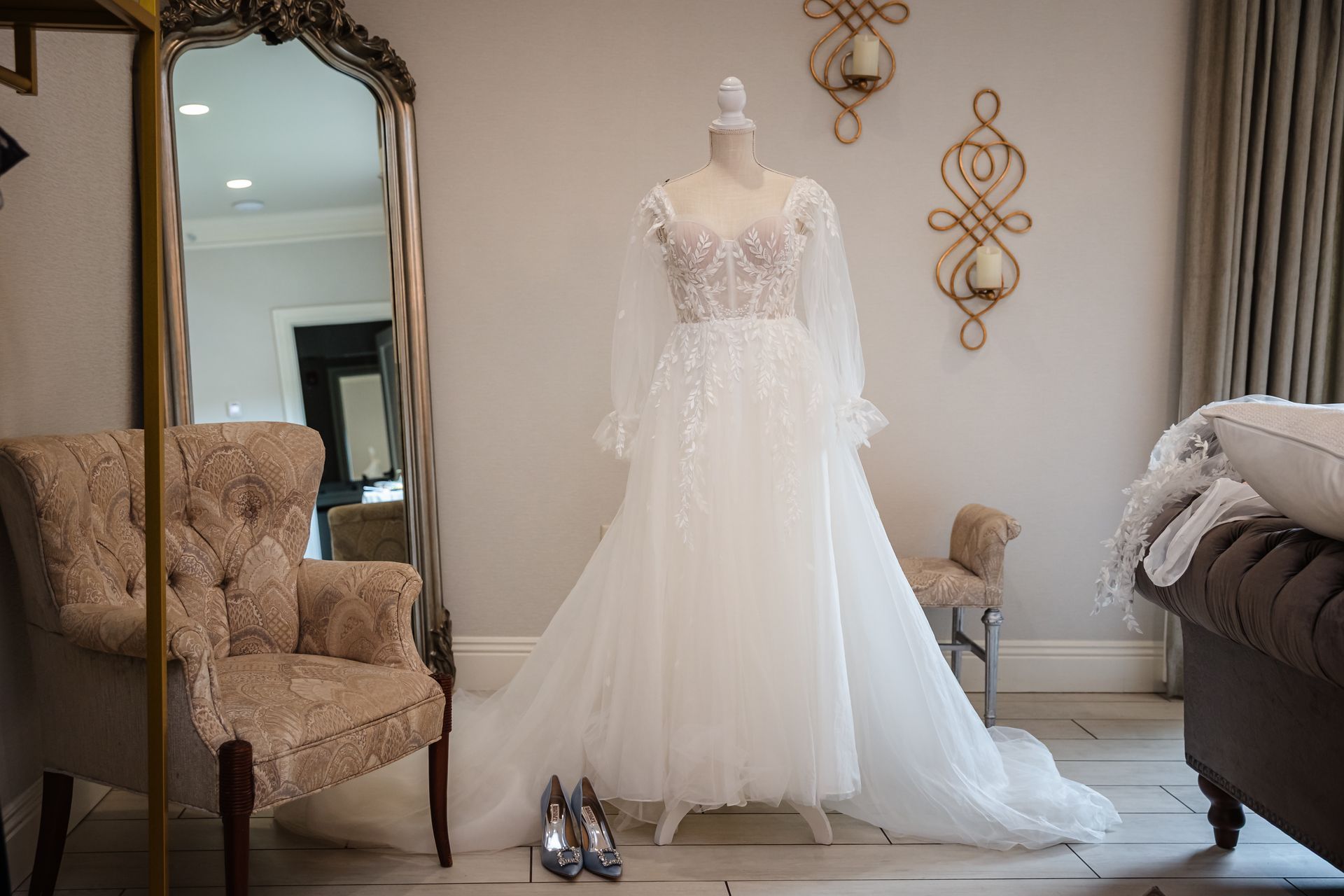 Wedding dress on a mannequin in a room with a large mirror, chair, and shoes.