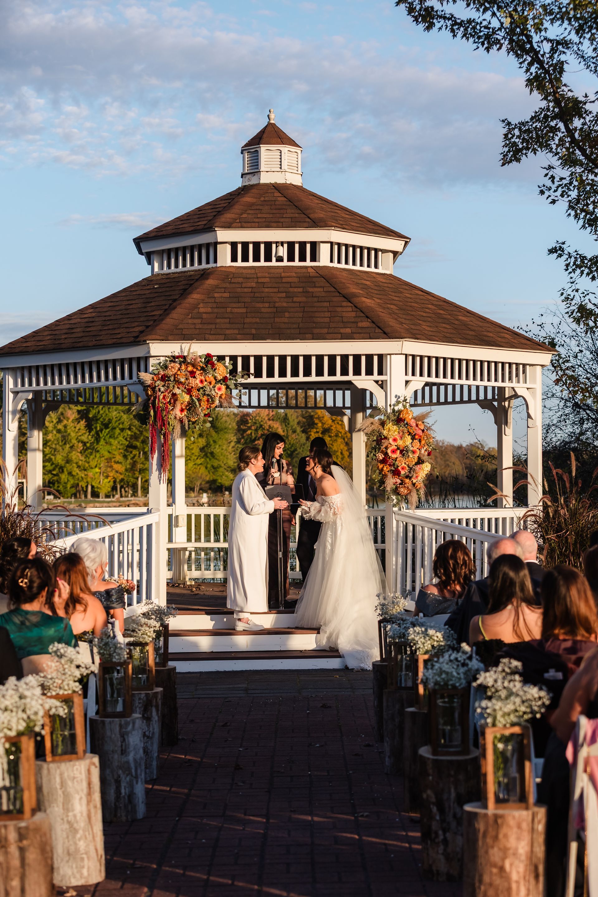 Wedding ceremony at gazebo with couple, guests, and floral decorations.