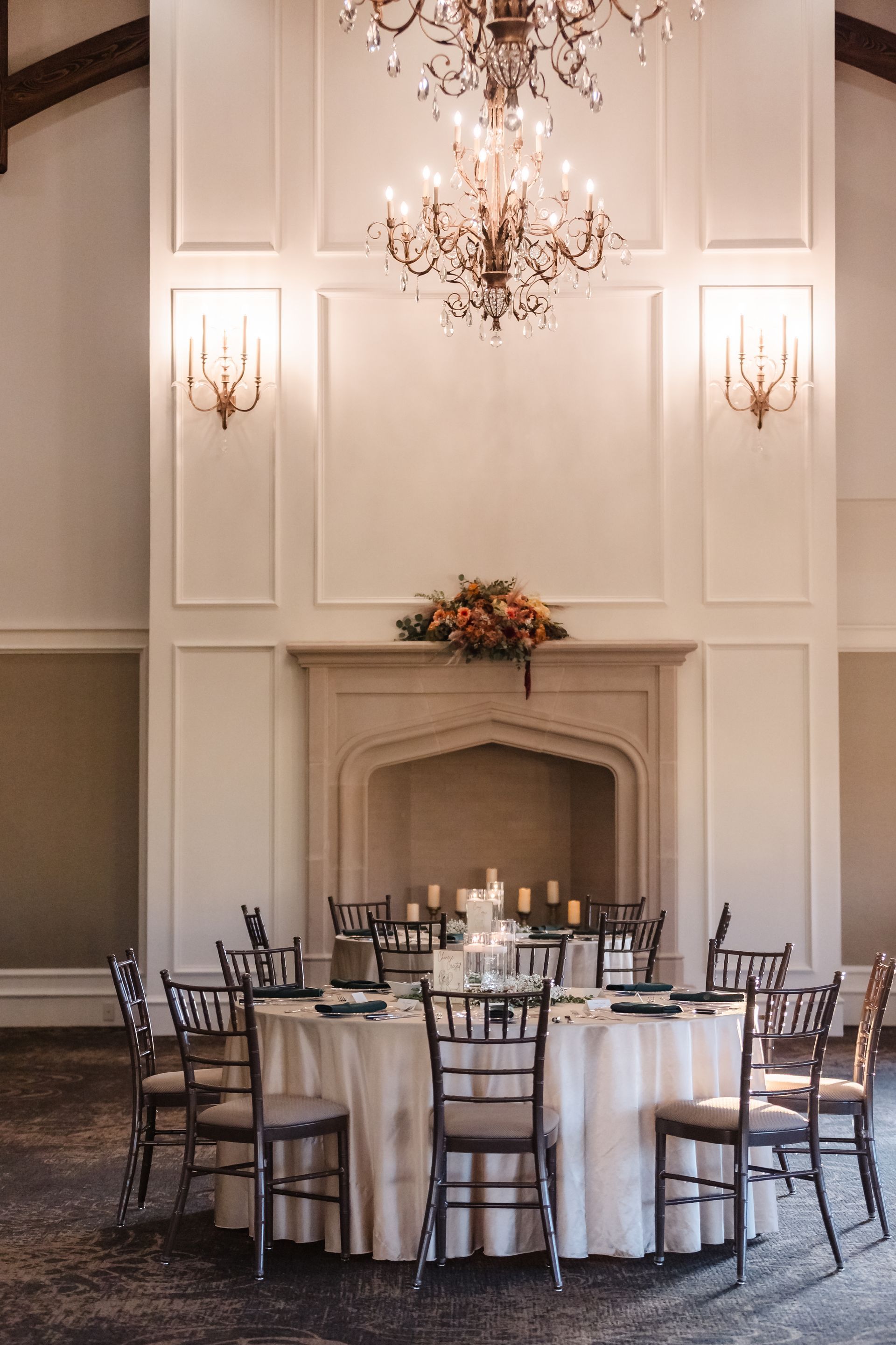 Elegant round table set for a formal event in a large room with a fireplace and chandelier.
