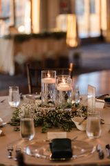 Table setting with floating candles, greenery, clear glasses, and place settings.