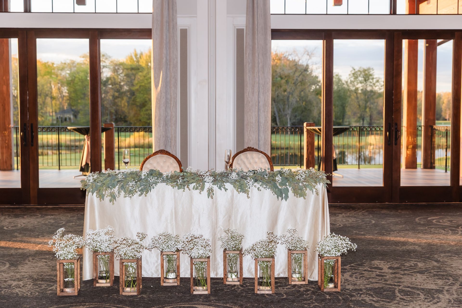 Wedding reception table set for two with floral arrangements, overlooking a lake.