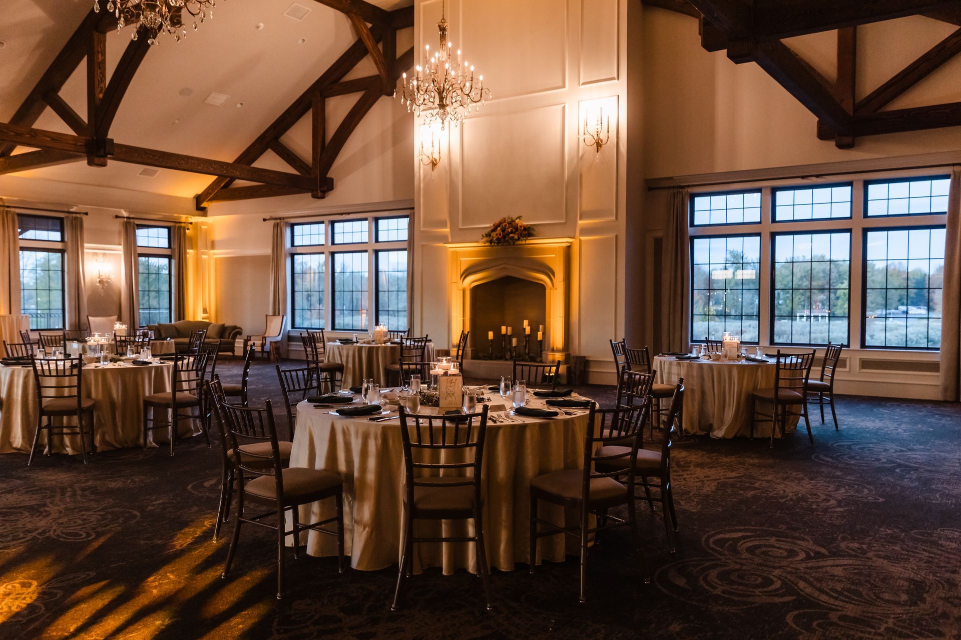 Elegant banquet hall with round tables set for a formal event. Fireplace and large windows.