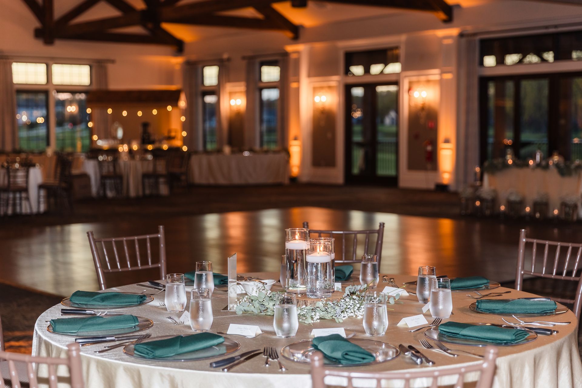 Round table set for a wedding reception, with teal napkins and centerpieces, in a warmly lit ballroom.