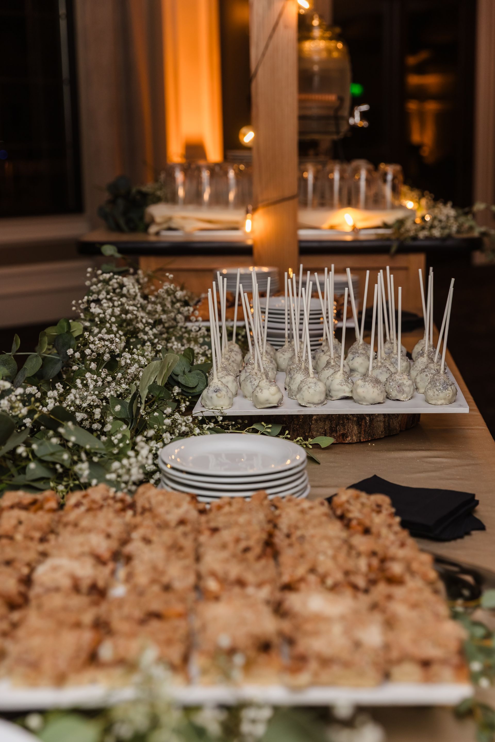 Dessert table with cake pops and cookies. Greenery and plates decorate the table.