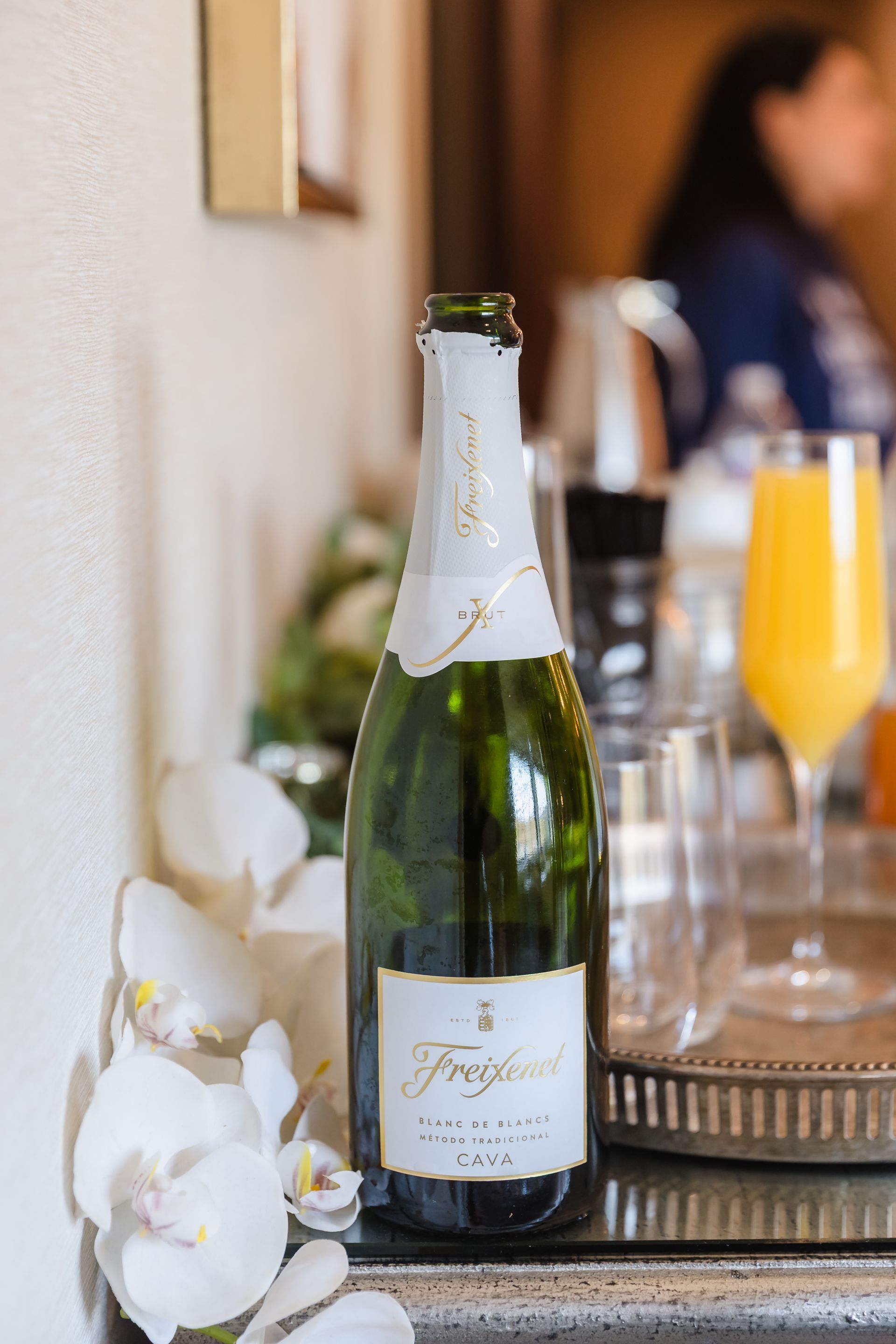A bottle of Freixenet champagne, orchids, and a mimosa on a tray.
