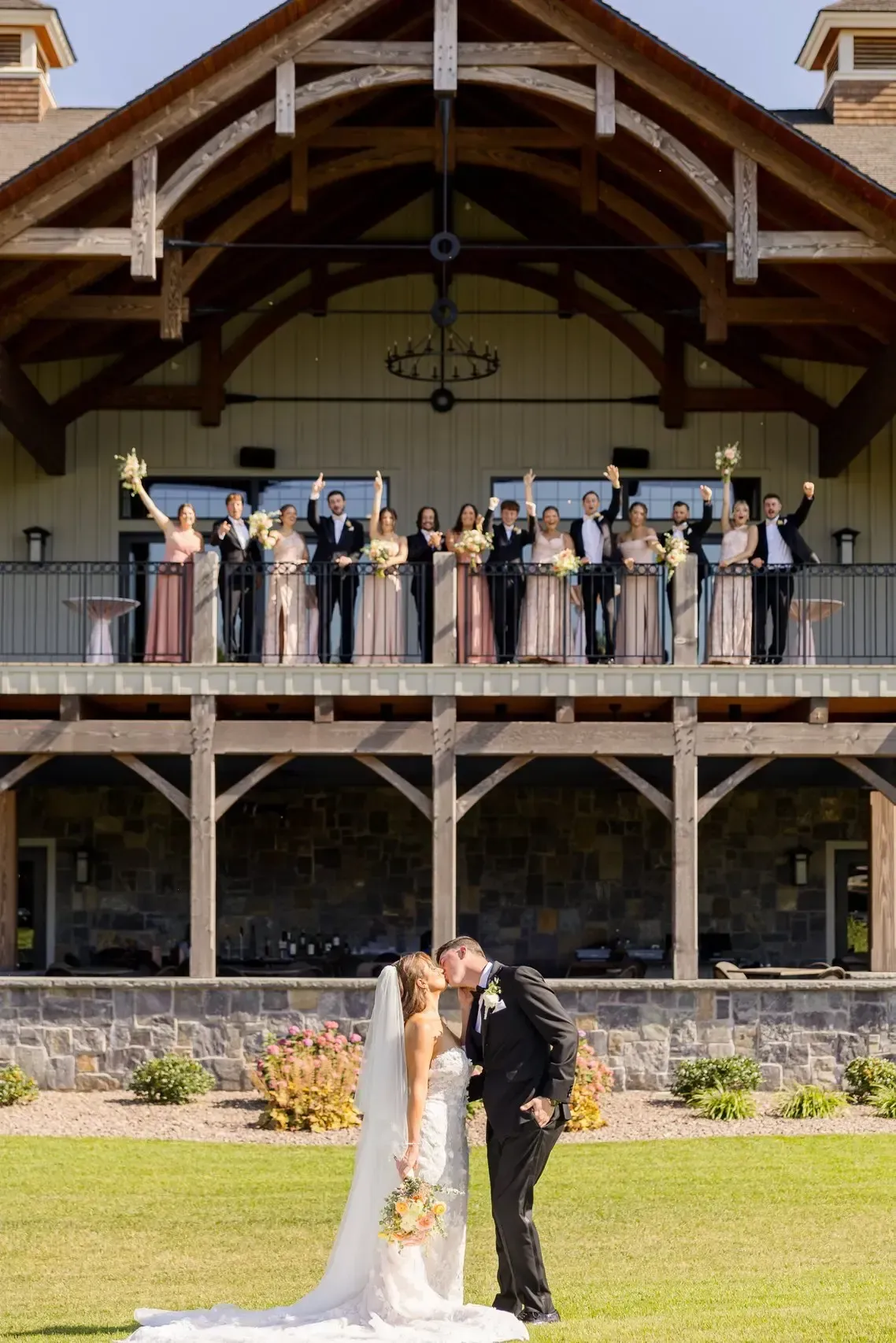 Couple kissing in front of wedding party on a two-story building's balcony.