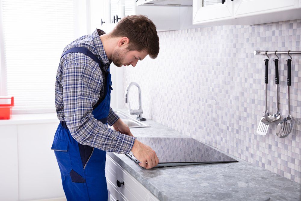 Repairman Installing Induction Stove In Kitchen — Mingleford Electrical Airconditioning Solar & Gas In Landsborough, QLD