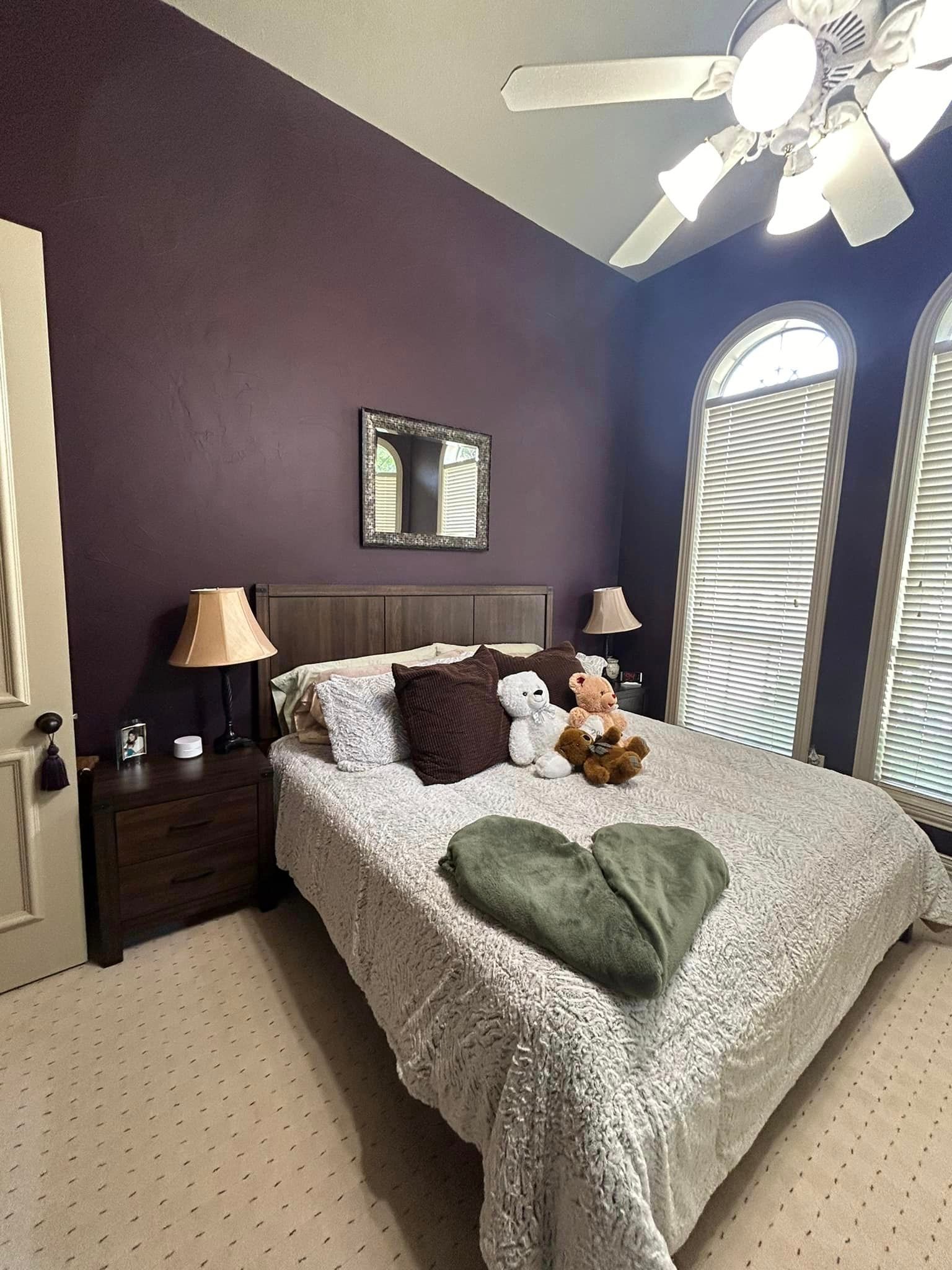 A bedroom with purple walls and a ceiling fan