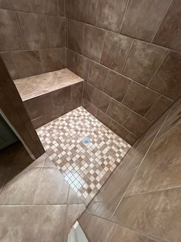 A walk in shower with brown tiles and a bench.