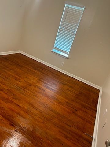An empty bedroom with hardwood floors and a window.