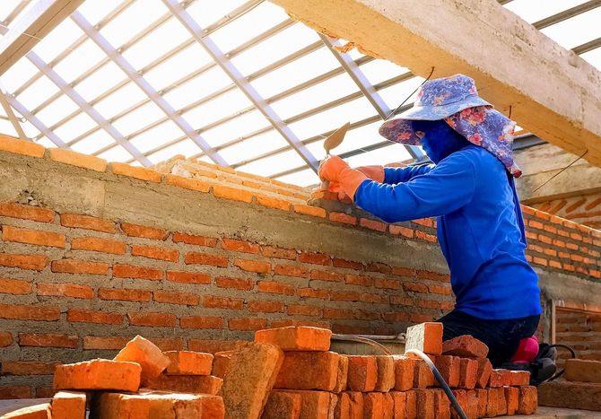 Worker in blue jacket and orange gloves installing roof panels on a brick building under construction