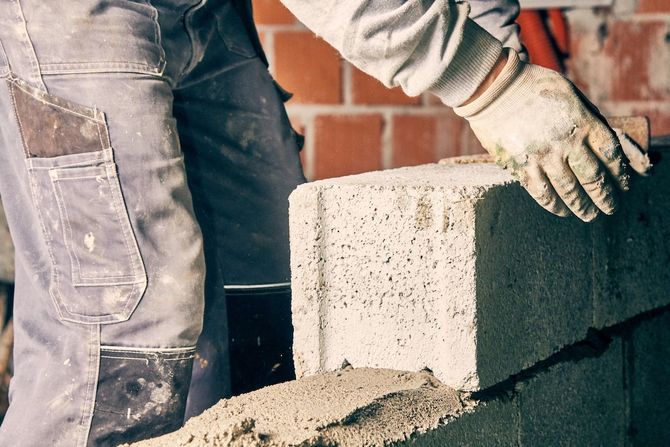Worker laying cinder blocks at a construction site beside a brick wall