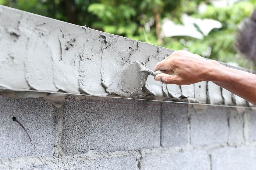 Hand smoothing wet concrete on a cinder block wall outdoors