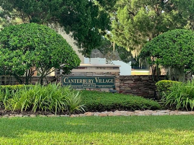A sign for canterbury village is surrounded by trees and bushes.