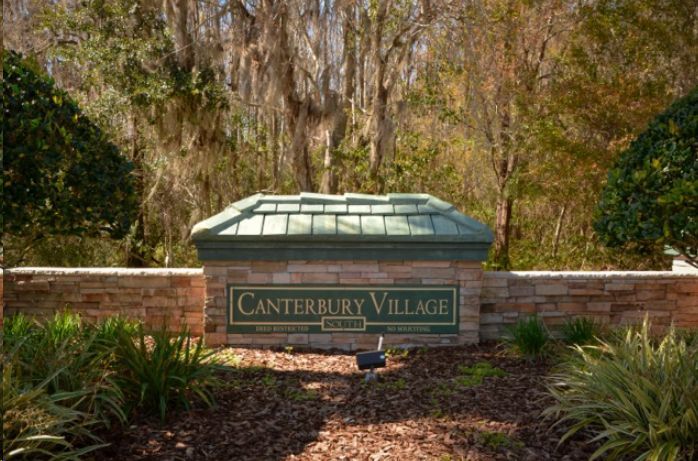 A sign for canterbury village is surrounded by trees and bushes.