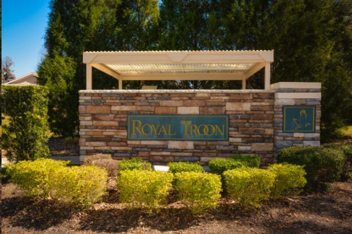 A stone wall with a sign that says royal throne on it surrounded by bushes and trees.