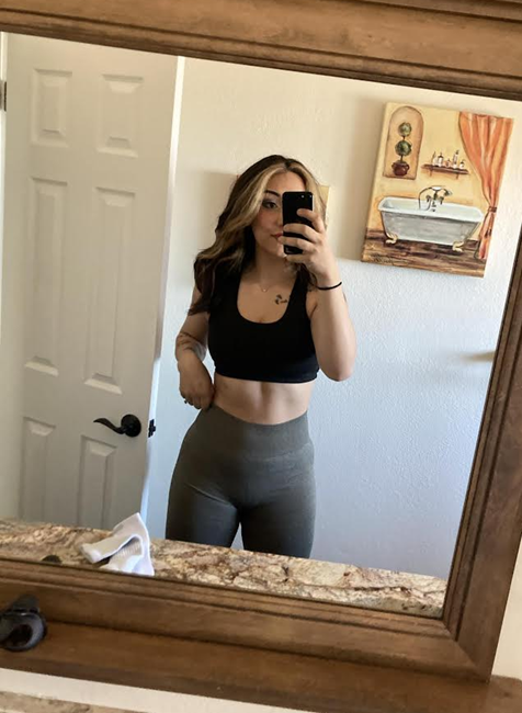 Woman in workout attire taking a mirror selfie in a bathroom, holding phone.