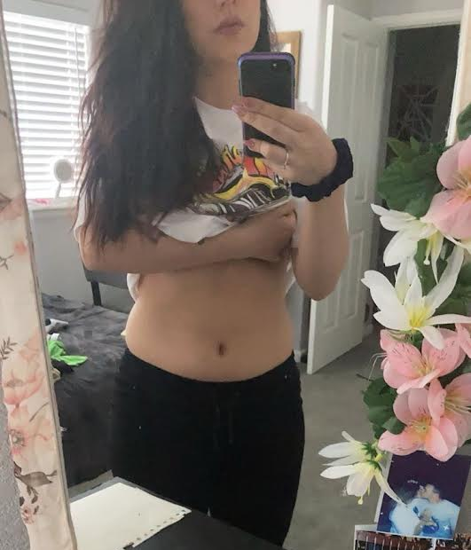 Woman in a white shirt and black pants takes a mirror selfie.