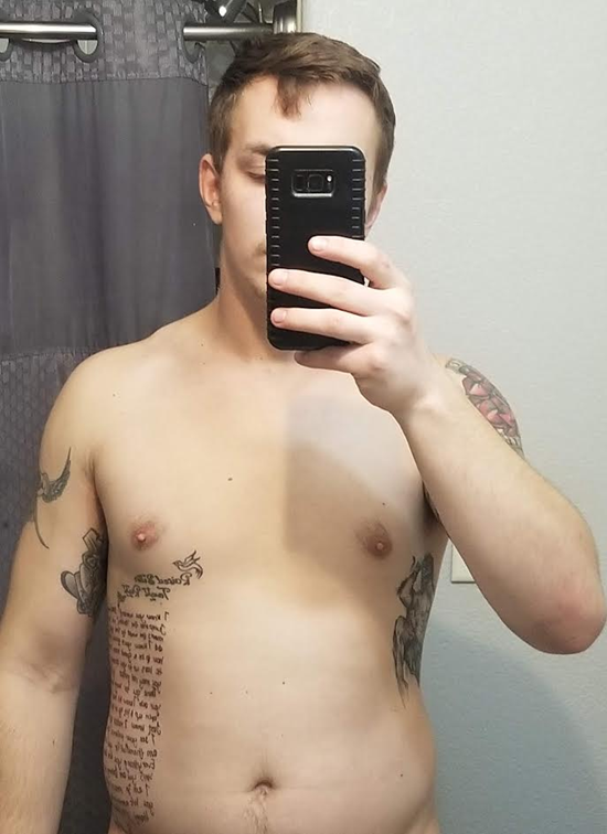 Man taking a mirror selfie, shirtless with tattoos, holding a phone. Bathroom setting.