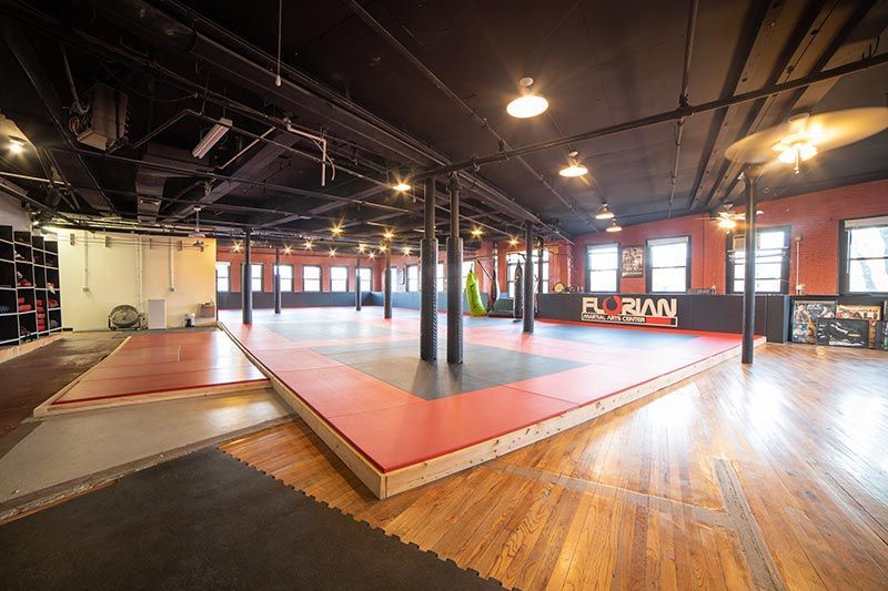 Spacious martial arts studio with red mats, wooden floors, and black ceiling beams