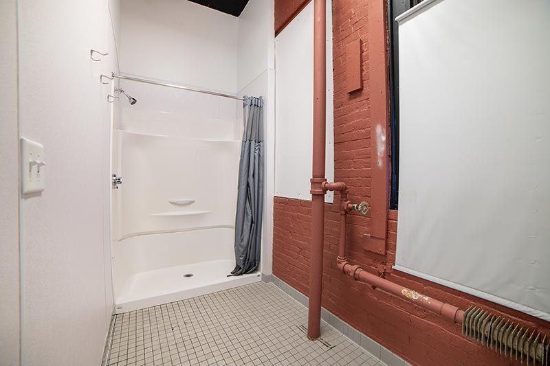 Accessible shower stall in a tiled bathroom with a handheld shower and red exposed piping
