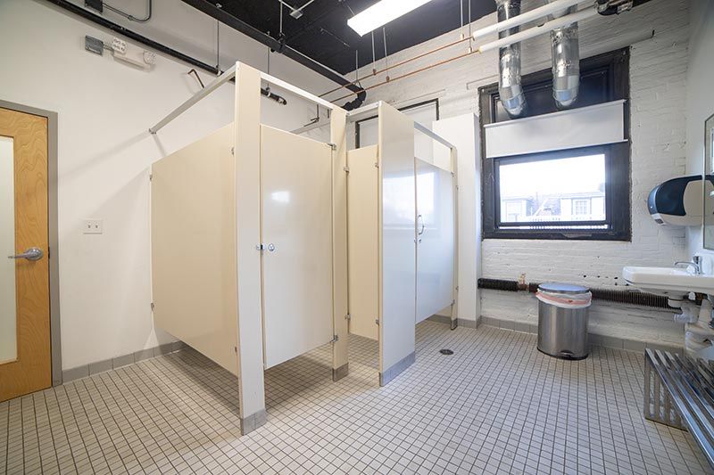 Public restroom interior with beige stalls, tiled floor, sinks, and a window overlooking the hallway