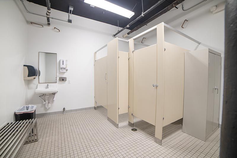 Public restroom with beige stalls, white walls, tiled floor, and sink area under fluorescent lights