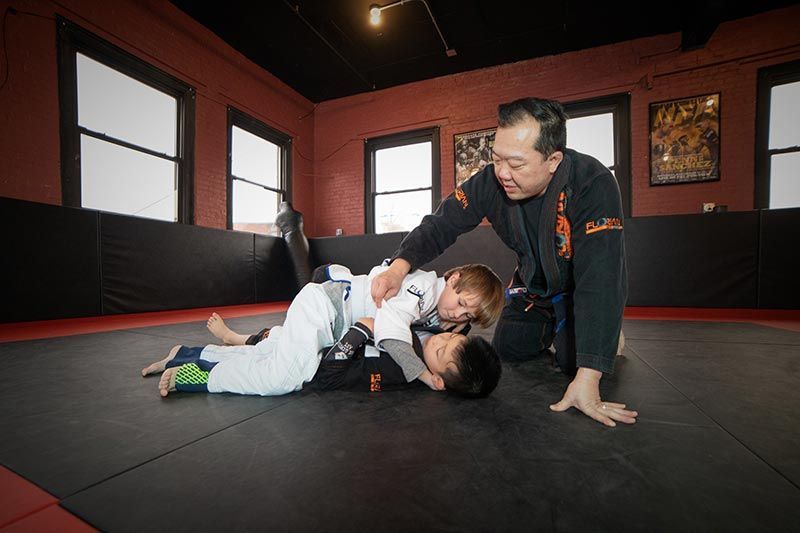 Martial arts instructor demonstrating a grappling move with a student on a mat in a training room