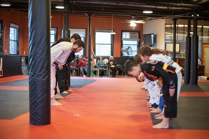 Children bowing in a martial arts dojo on orange mats, facing an instructor.